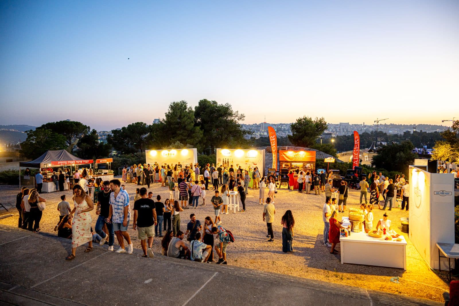 Crowd gathered at an outdoor community festival at sunset with string lights